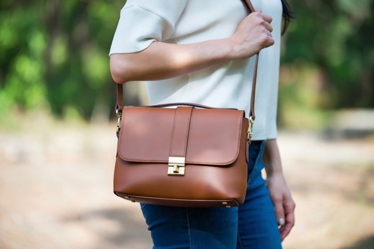 Person holding a brown leather bag outdoors